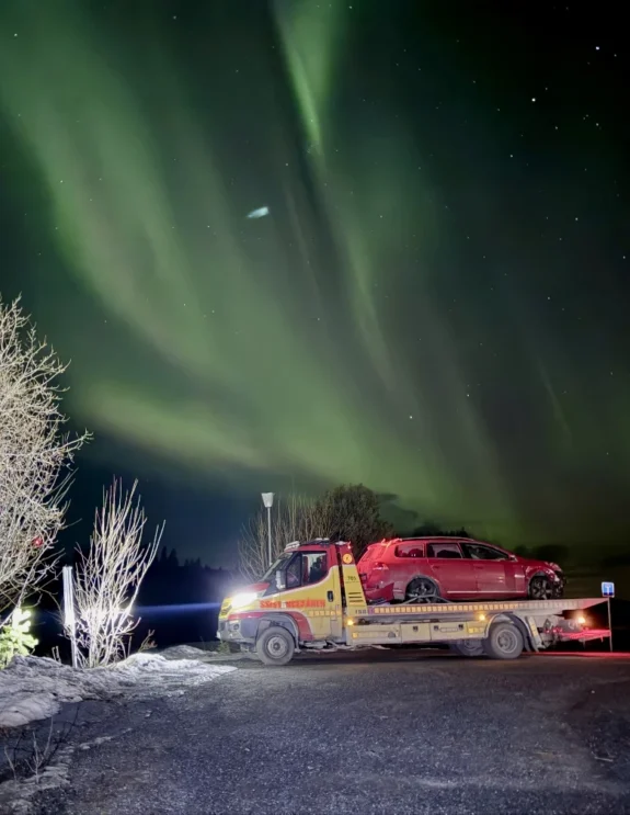 En bärgningsbil från Årebärgarn som transporterar en bil nattetid under ett grönt norrsken.